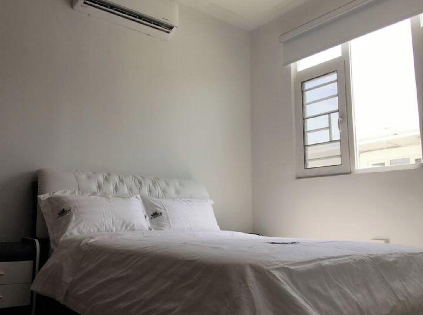 A bedroom with a bed, a nightstand, and a window.