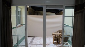 Una stanza con una porta vetrata scorrevole che dà su un balcone con pavimento piastrellato e sedie in vimini.