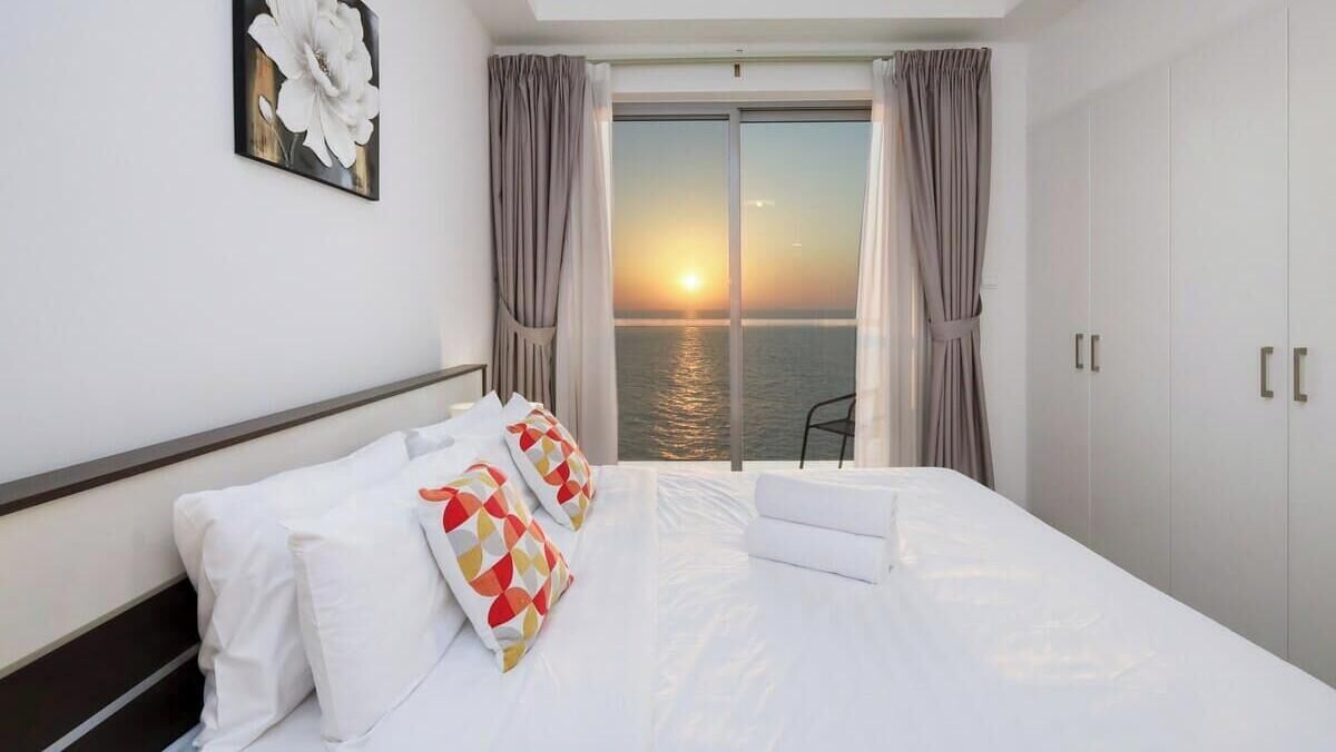 Una camera d'albergo con un letto, vista del tramonto sull'acqua e un balcone con una sedia.
