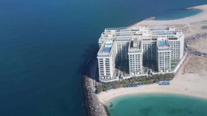 A high-rise hotel with multiple balconies, situated by a beach with clear waters.