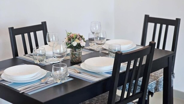 A dining table set with plates, glasses, and cutlery, surrounded by chairs.