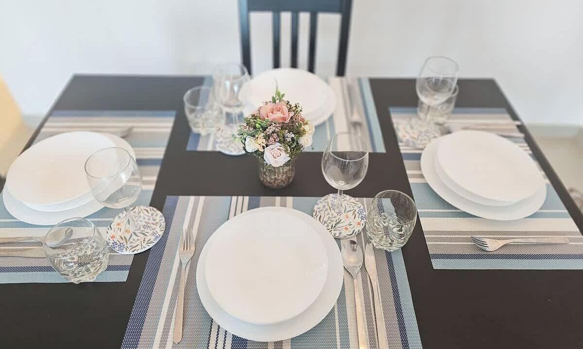 Una tavola imbandita con piatti, bicchieri e posate, decorata con un'elegante composizione floreale.