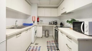 A compact kitchen with a washing machine, a microwave, a coffee maker, and a trash bin.