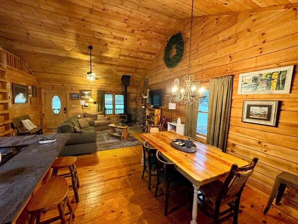 Un interior acogedor de cabaña con una mesa de comedor de madera, sillas, un sofá y una chimenea.