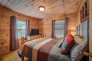Ein Schlafzimmer einer Holzhütte mit Bett, Vorhängen, einem Fernseher und einem Fenster.