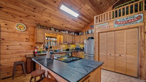 Cocina de cabaña de madera con una isla central, taburetes de bar, un reloj y letreros de alquiler de canoa.