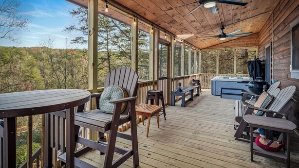 Una terraza techada con piso de madera, sillas Adirondack, una mesa redonda y un ventilador de techo.