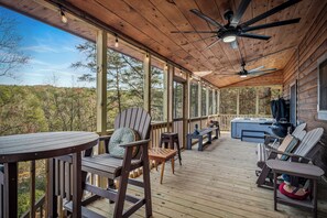 Una terraza techada con piso de madera, sillas Adirondack, una mesa redonda y un ventilador de techo.