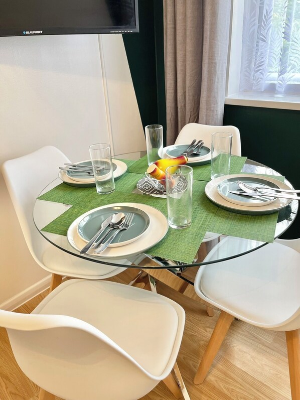 A dining area with a glass table, white chairs, and a green table runner.