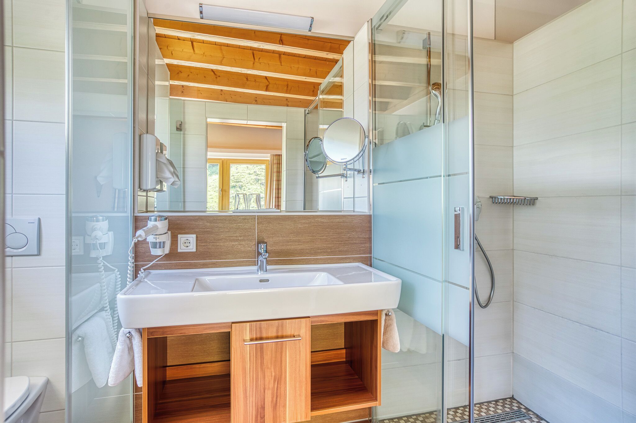 A modern bathroom with a wooden vanity, a large mirror, and a glass shower enclosure.