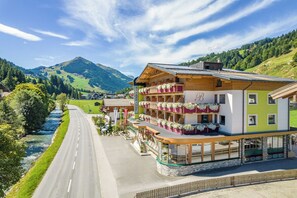 Ein mehrstöckiges Hotel mit Balkonen, einem Fluss und Bergen im Hintergrund.