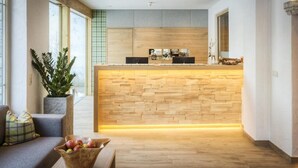 A modern kitchen with a wooden island, a sofa, and a coffee table with apples. - Hotel Barbarahof (Saalbach-Hinterglemm)