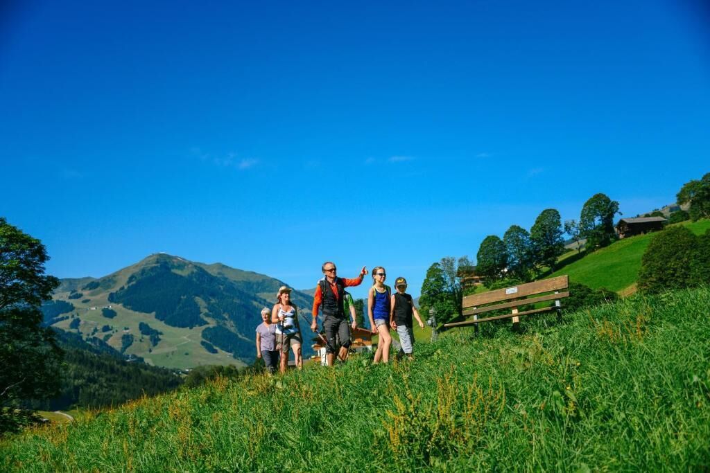 Un grupo de personas en una colina cubierta de hierba, con una montaña al fondo y un banco de madera.