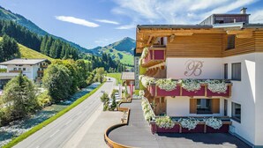 A hotel with a prominent 'BARBARA' sign, wooden balconies with flowers, a river view, and a mountainous backdrop. - Hotel Barbarahof (Saalbach-Hinterglemm)