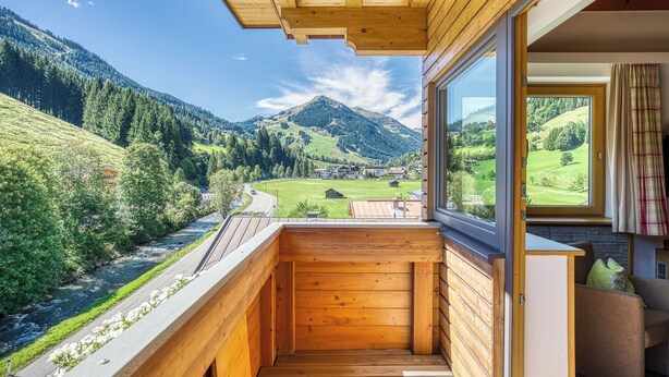 A wooden balcony with a view of a river and mountains. - Hotel Barbarahof (Saalbach-Hinterglemm)