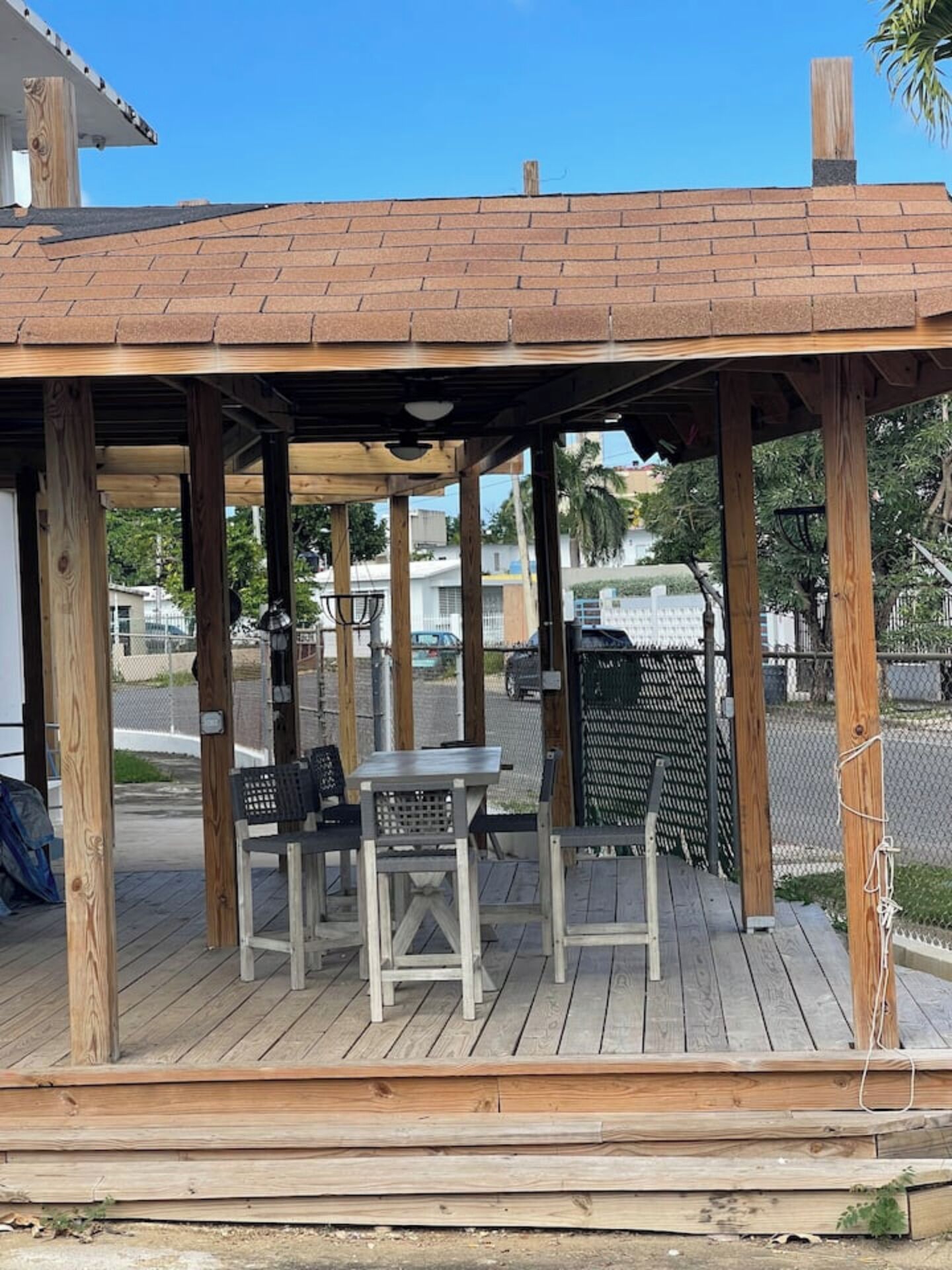 Une terrasse en bois dotée d’un espace salon couvert, comprenant une table et des chaises, le tout abrité par un toit en tuiles.