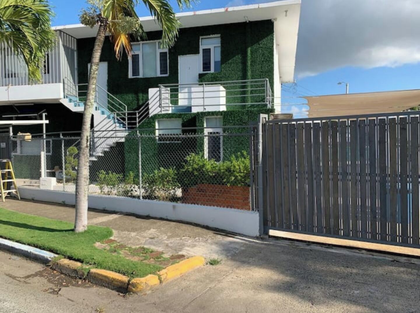 A modern two-story building with a green facade, a metal fence, and a gated entrance.