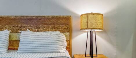 A bed with striped pillows and a wooden headboard, a bedside table with a lamp, and a small drawer.