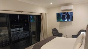 Une chambre d’hôtel dotée d’un grand lit, d’un téléviseur fixé au mur, d’un balcon avec une porte vitrée et d’un coin salon avec des fauteuils.