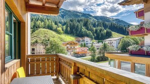 Un balcón de madera con una mesa y sillas, con vistas a un pueblo montañoso con casas y vegetación.