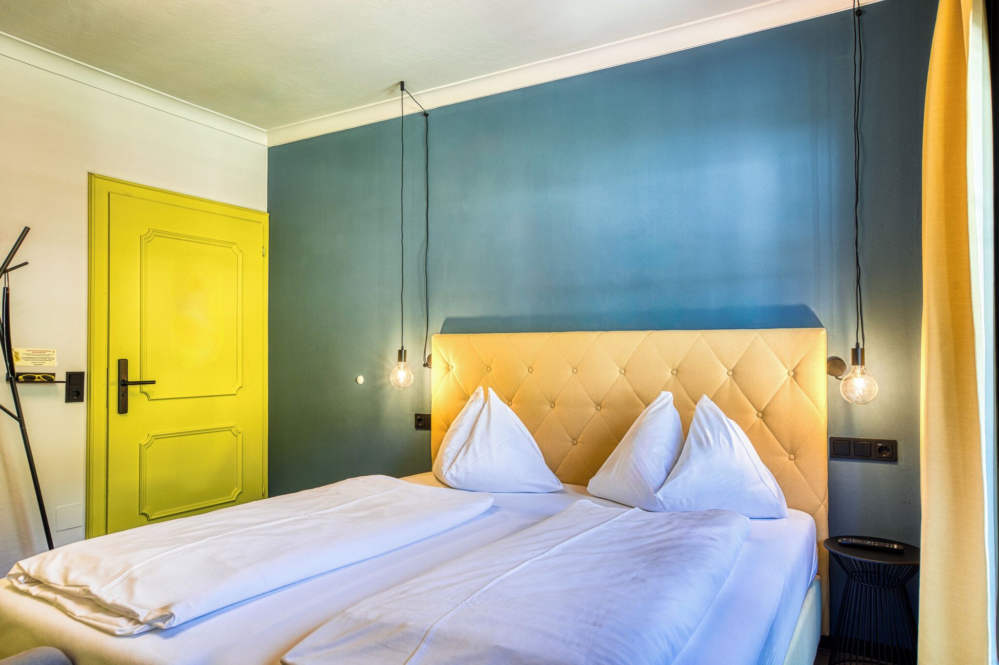 A hotel room with a bed, a yellow door, and a blue wall.