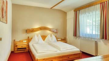 Ein Hotelzimmer mit einem hölzernen Bett, einem Nachttisch, Vorhängen an einem Fenster und einer Heizung.