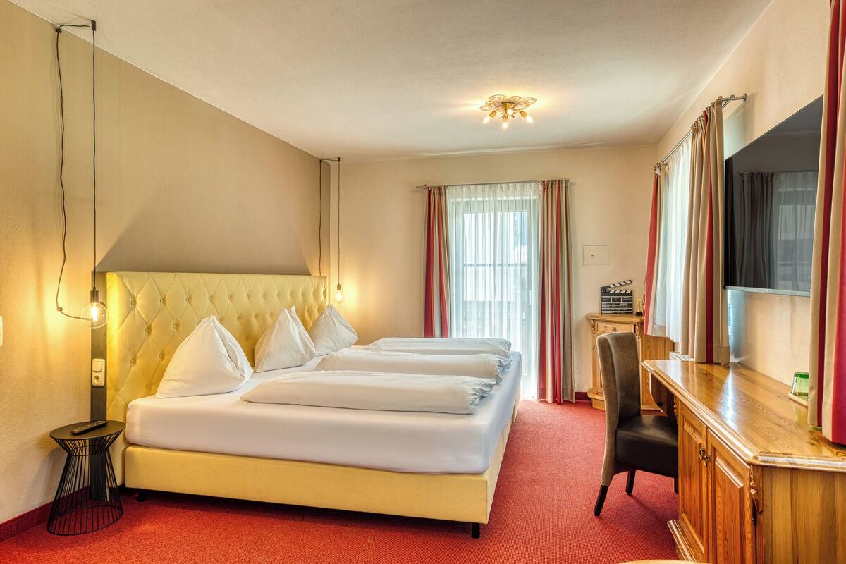 Une chambre d’hôtel avec un grand lit, un bureau, une chaise, une télévision et une fenêtre avec des rideaux.