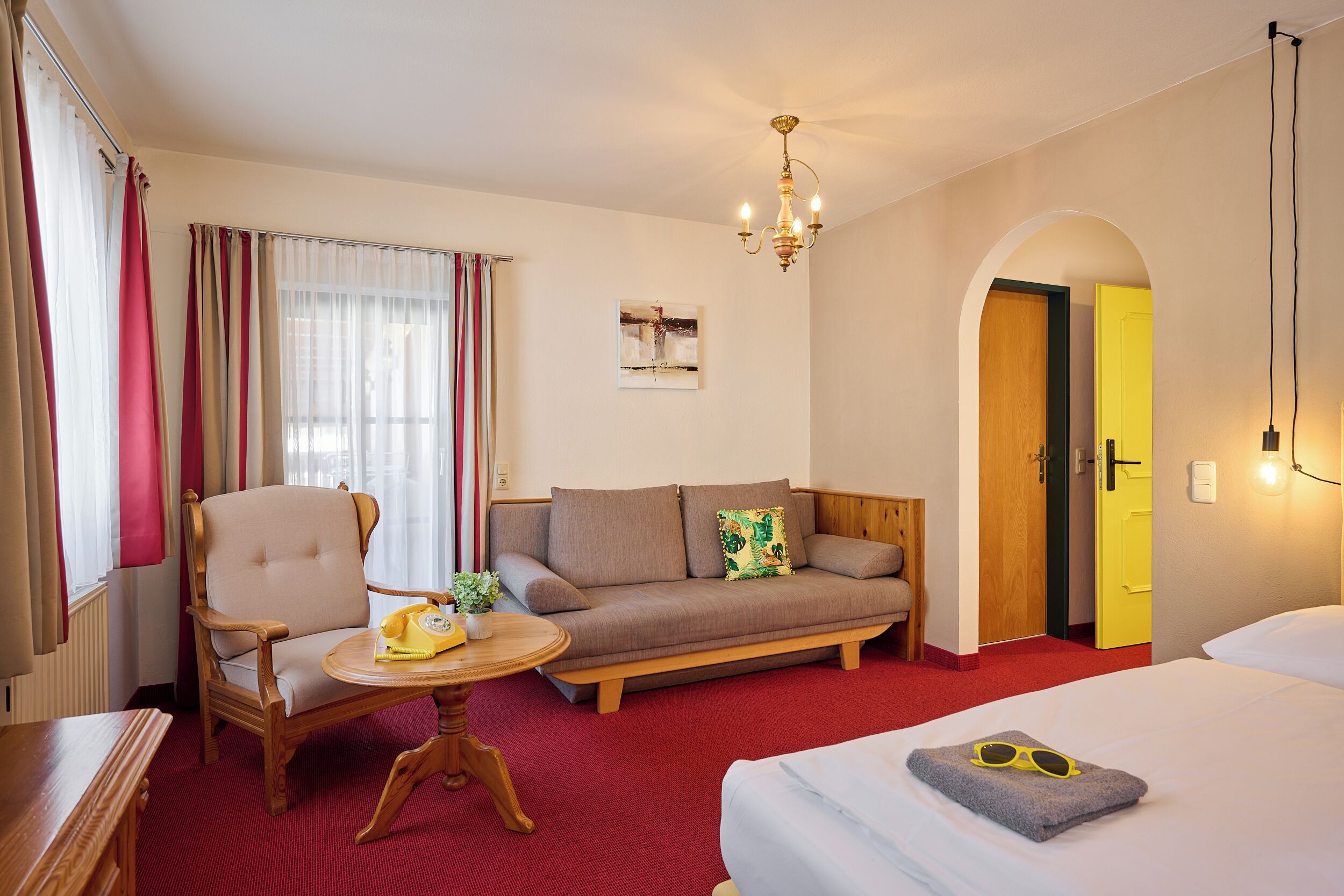 A hotel room with a bed, a sofa, a chair, a small table, and a window with curtains.