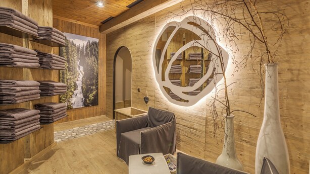 Un interior de madera con chimenea, un toallero de pared, una zona de estar con cojines y un espejo decorativo.