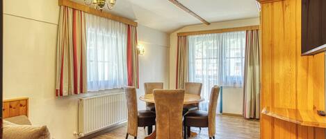 A cozy living room with a wooden dining table, comfortable seating, a radiator, and a television on a wooden stand.