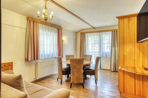 Una sala de estar acogedora con una mesa de comedor de madera, asientos cómodos, un radiador y un televisor sobre un mueble de madera.