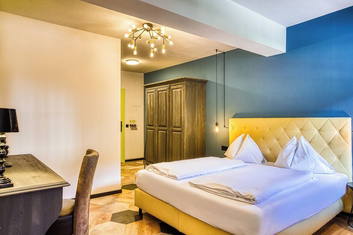 Une chambre d’hôtel comprenant un lit, une table de chevet, une lampe, une armoire et un lustre.