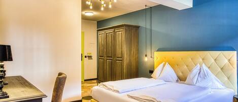 A hotel room with a bed, bedside table, lamp, wardrobe, and a chandelier.
