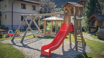 A playground with a red slide, wooden climbing structures, and a small gazebo.