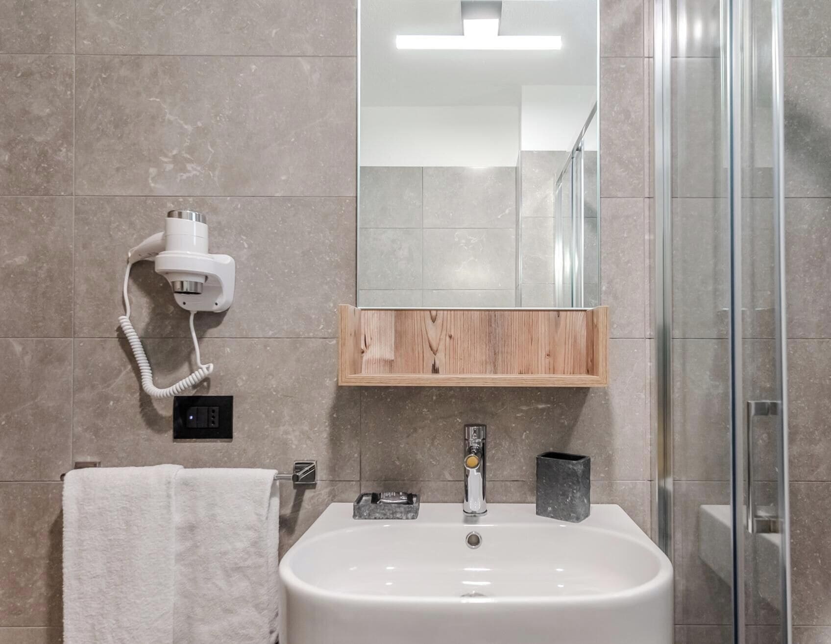 Een badkamer met een wit wastafelmeubel, een spiegel, een houten plankje, een handdoek en een douche.