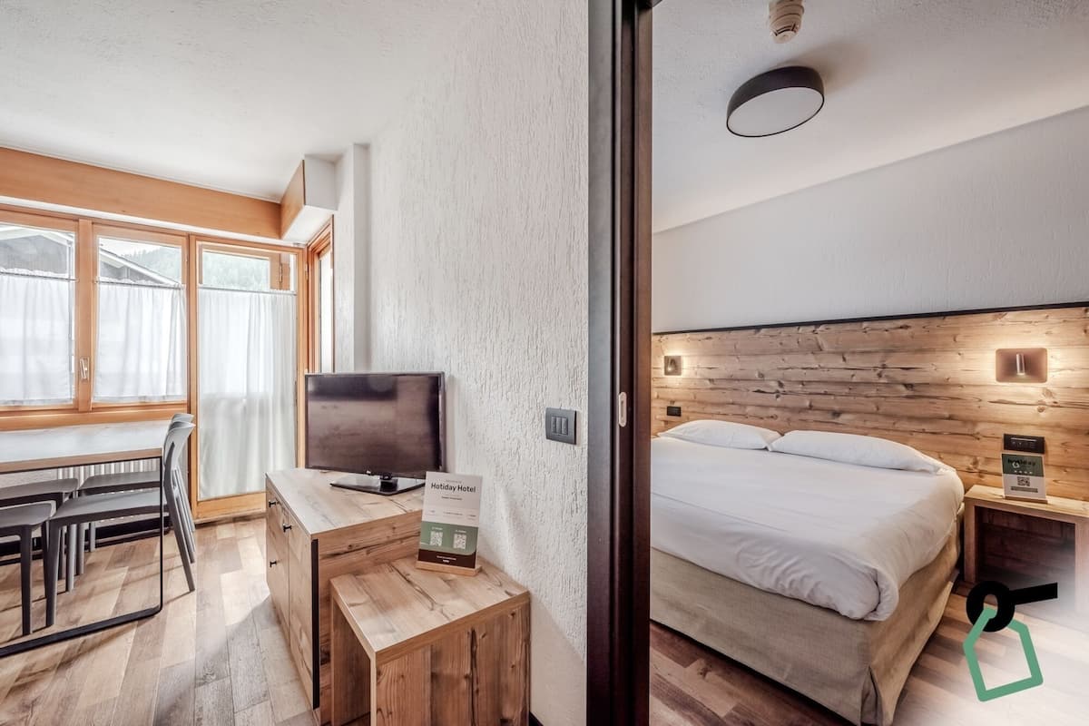 Moderni hotellihuone, jossa on puinen sängynpääty, sänky, työpöytä, jossa on televisio, ja pieni pöytä.