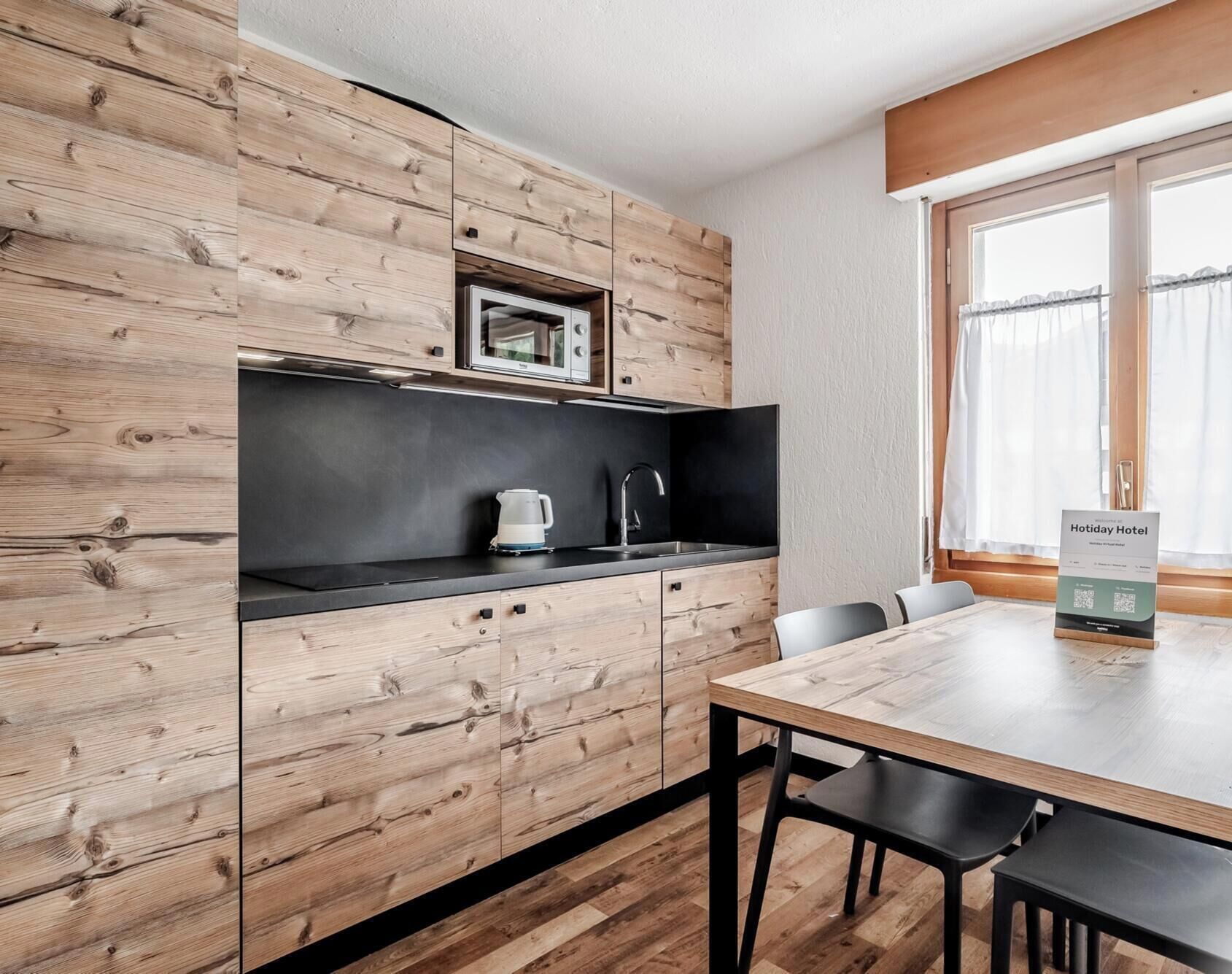 Una cocina moderna con armarios de madera, encimera negra, hervidor y un comedor con mesa y sillas.
