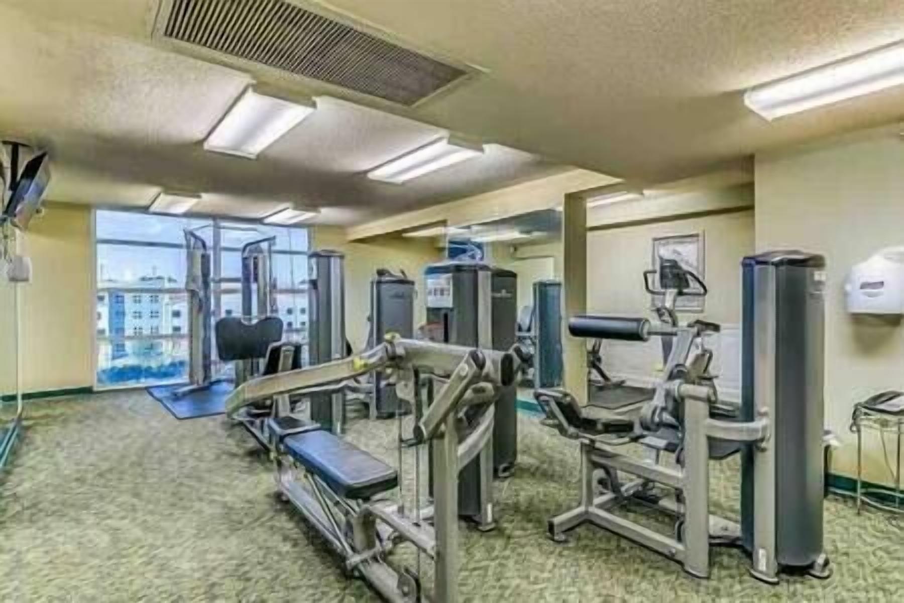 A gym with various exercise machines, a large window, and a view of buildings outside.