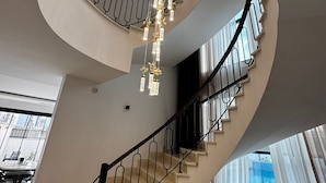 En spiraltrappa i flera våningar med en modern design, utrustad med ett svart räcke och en kristallkrona med hängande lampor.