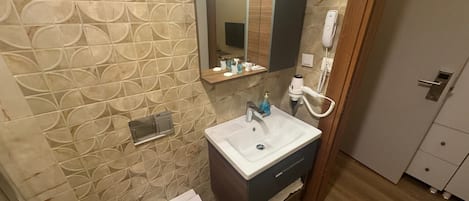 Une salle de bain avec un mur à motifs, un lavabo avec un miroir au-dessus, des toilettes et une porte portant un numéro.