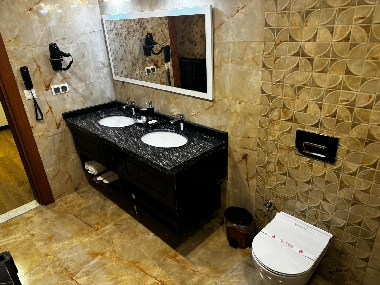 Een badkamer met twee wastafels, een spiegel, een toilet en een prullenbak.