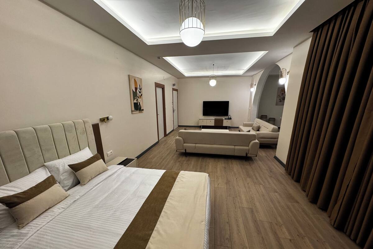 Ein modernes Hotelzimmer mit einem großen Bett, einer Couch, einem Fernseher und einer Deckenleuchte.