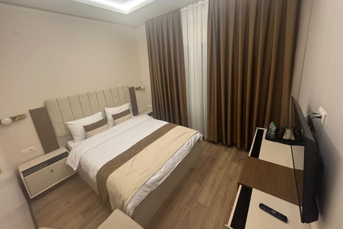 Ein Hotelzimmer mit Bett, Nachttischen, einem Fernseher und Vorhängen.