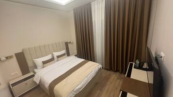 Ein Hotelzimmer mit Bett, Nachttischen, einem Fernseher und Vorhängen.
