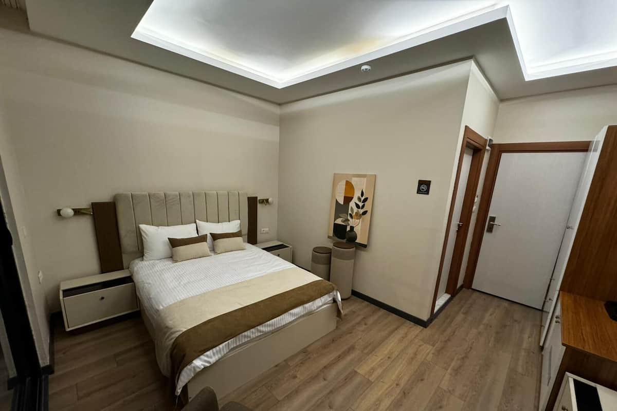 Ein Schlafzimmer mit Bett, Nachttischen, einem Wandbild und einer Tür.