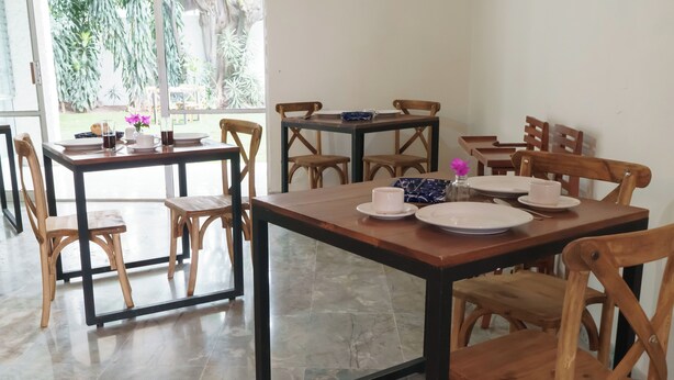 A dining area with wooden tables and chairs, a glass partition, and a view of greenery outside. - Estancia monraz (Guadalajara)