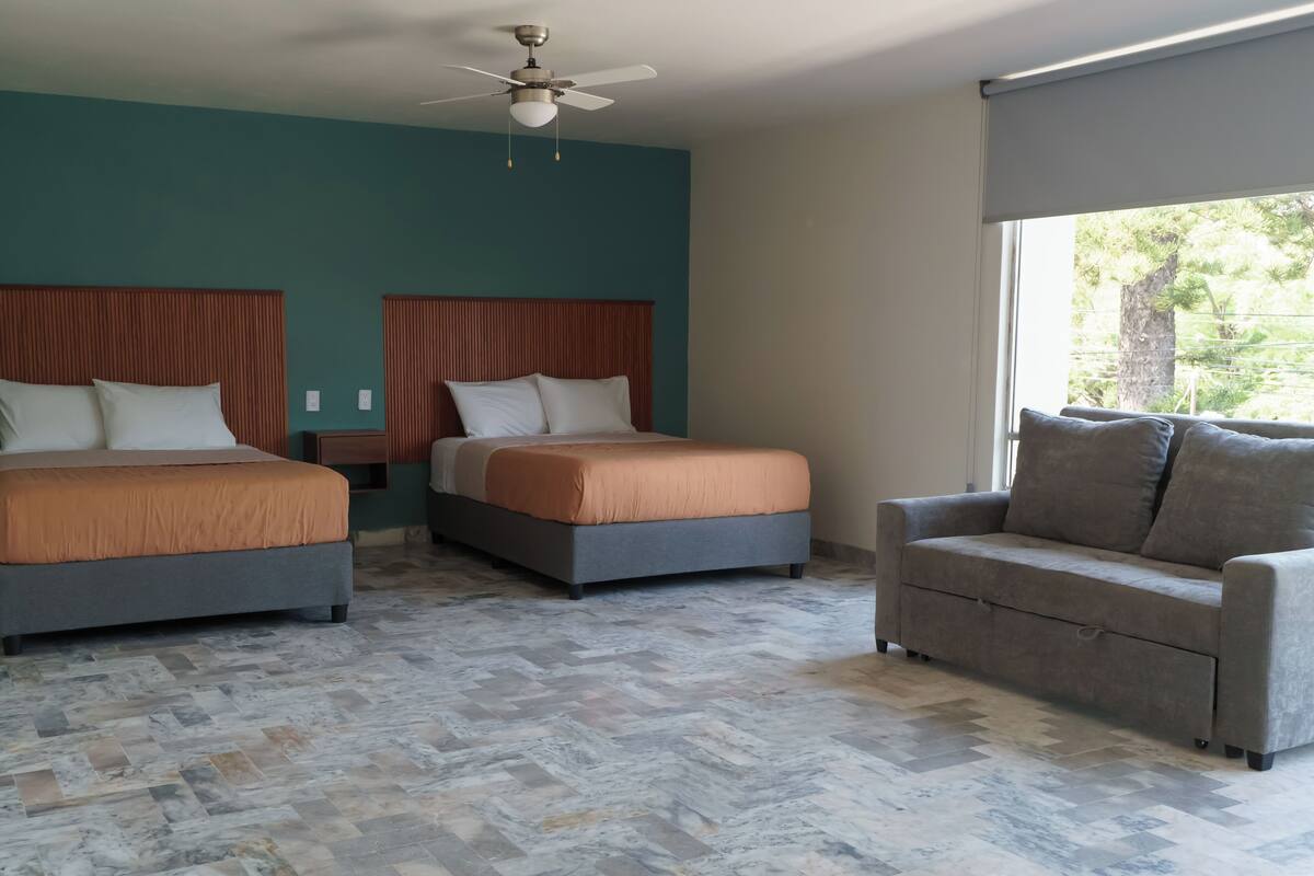 A hotel room with two beds, a sofa, a ceiling fan, and a large window.