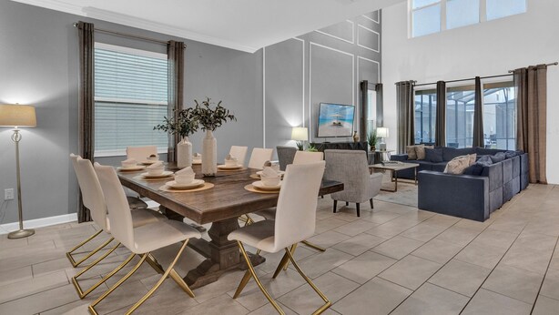 Un salon moderne doté d’un grand canapé d’angle, d’un coin repas avec une table et des chaises en bois, et d’un téléviseur fixé au mur.