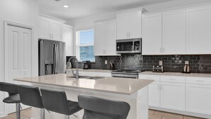 Una cocina moderna con armarios blancos, un refrigerador de acero inoxidable, un microondas y una isla grande con taburetes de bar.