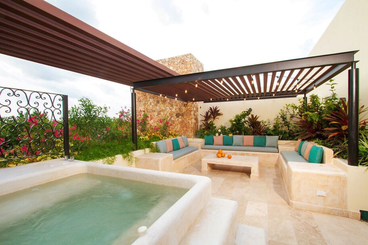 A covered outdoor seating area with a hot tub, stone wall, and potted plants.